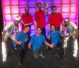 A group of 8 men in red and blue shirts, and white pants and a light-up backdrop.