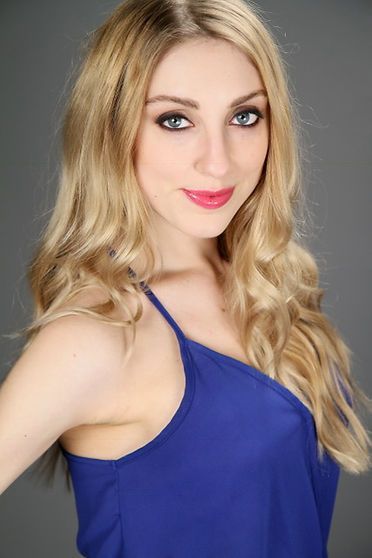 Blonde woman with blue eyes and red lipstick wearing a blue top, smiling.