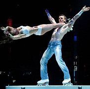 Acrobats on roller skates perform a balancing act on a stage, the man holding a woman in a horizontal pose.