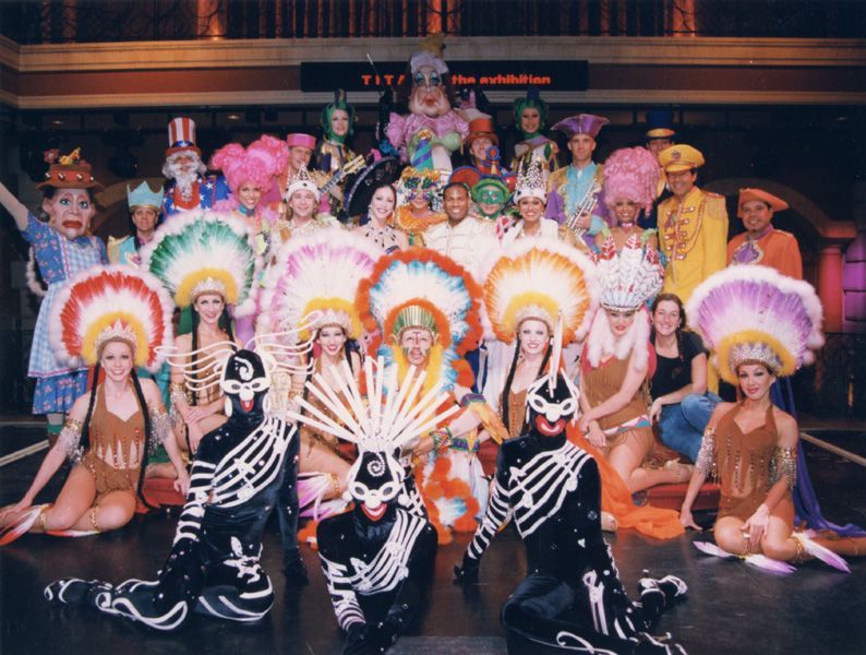 Dancers in elaborate costumes posing on stage. Various headdresses and skeletal outfits.