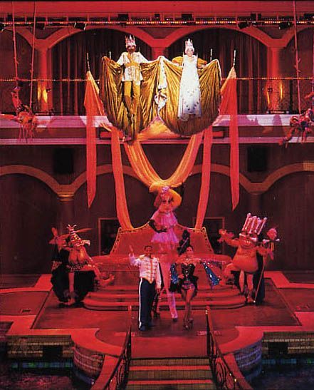 Stage performance with dancers and figures suspended in the air, lit in red.