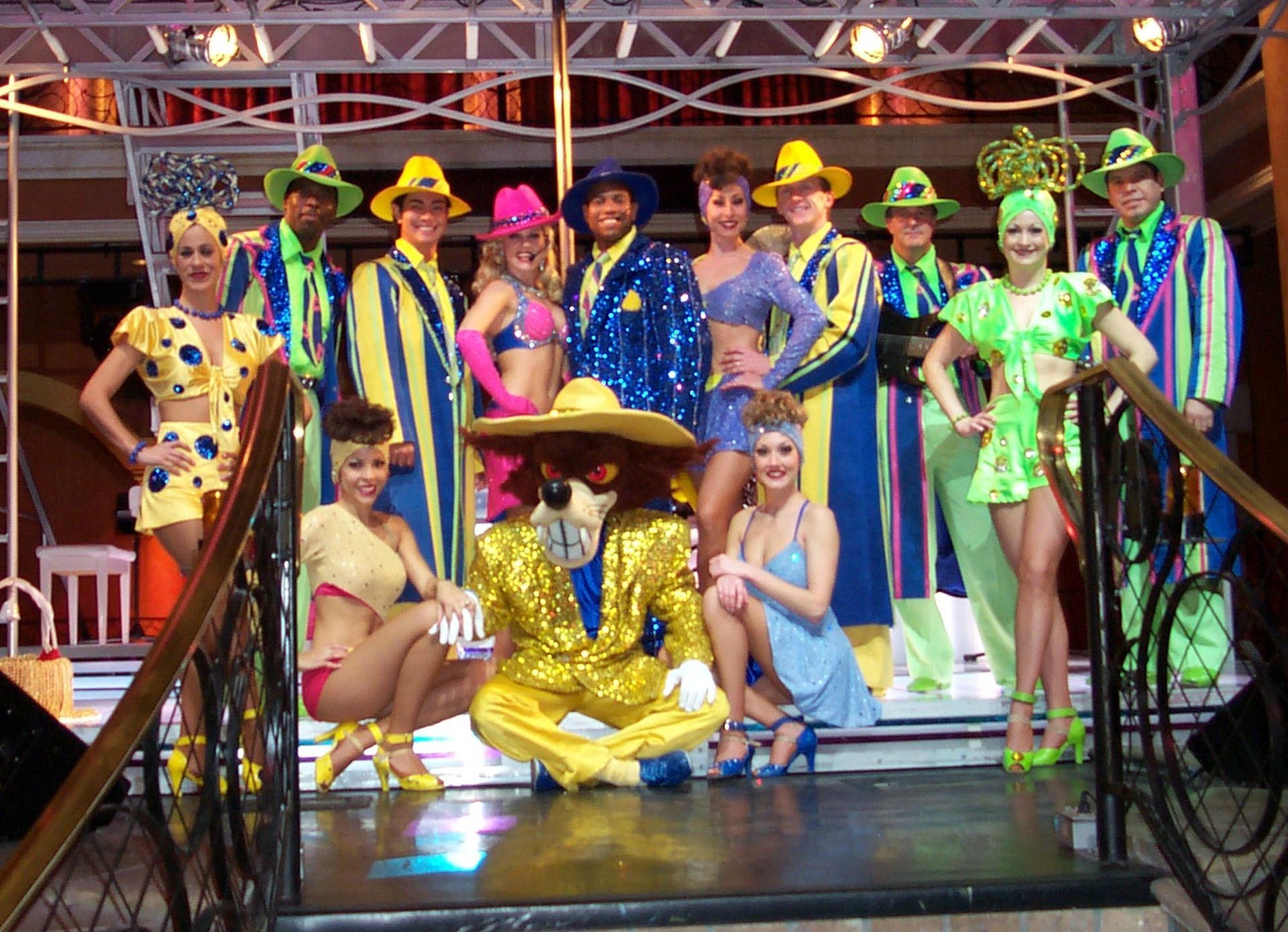 A group of performers in colorful costumes posing on a stage with a lion mascot.