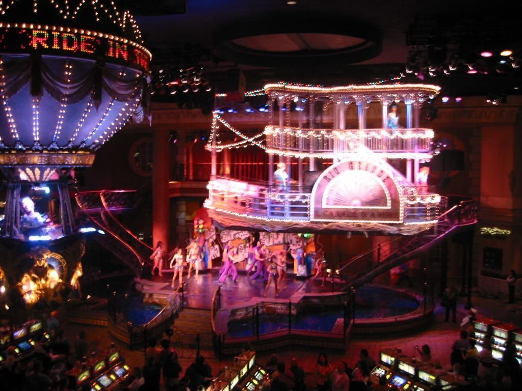 Showgirls on stage in front of a riverboat in a casino, with an air balloon to the left.