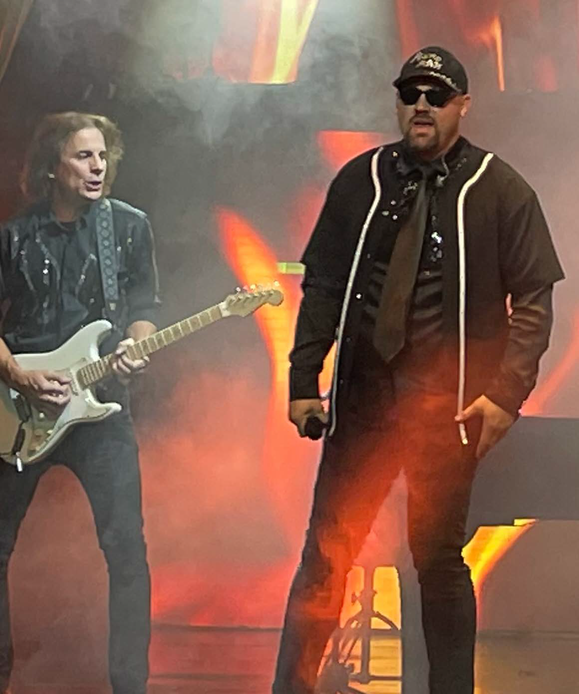 Two men on stage; one plays guitar, the other sings. Stage is lit with orange and red lights.