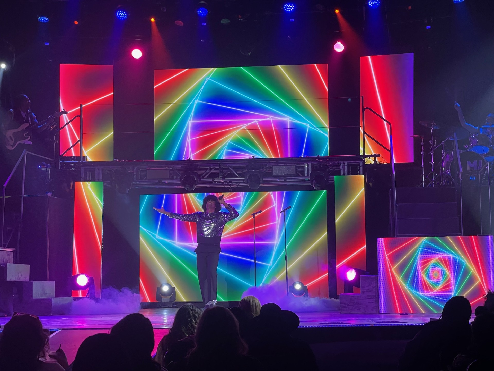 Performer on stage with rainbow-colored geometric light display.