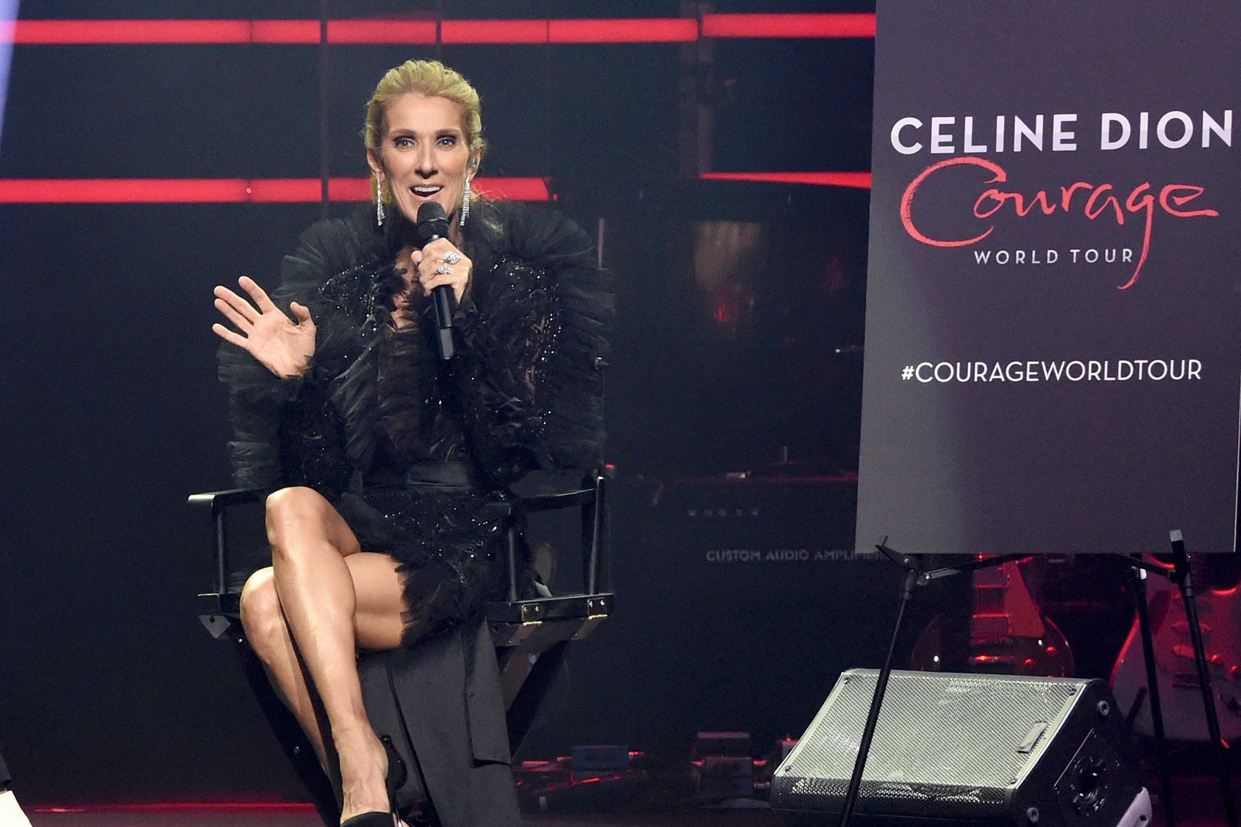 Celine Dion on stage, speaking into a microphone, wearing black, with the