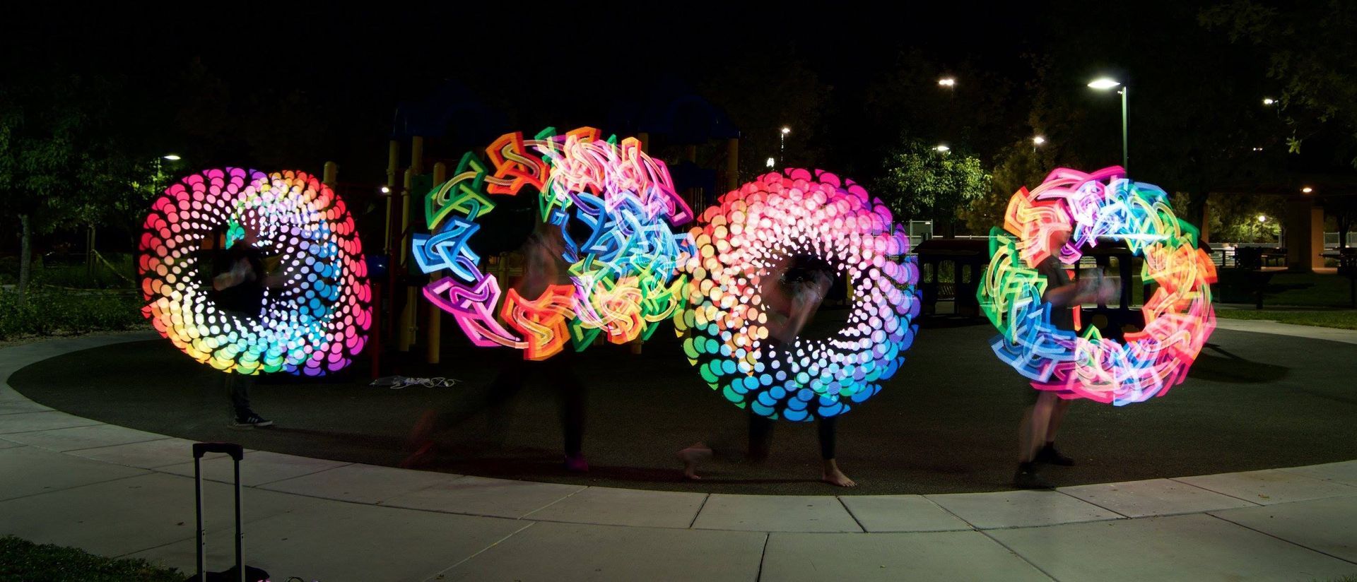Four people performing with colorfully lit, spinning hoops at night.