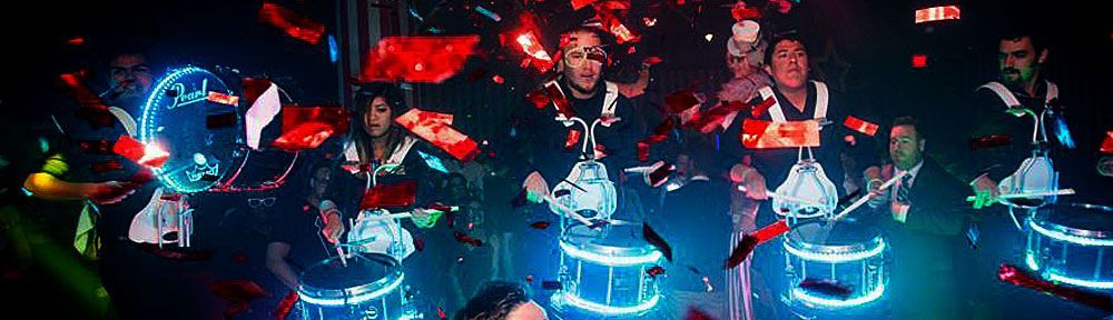 A drum group performing with glowing drums and confetti falling in a dark space.