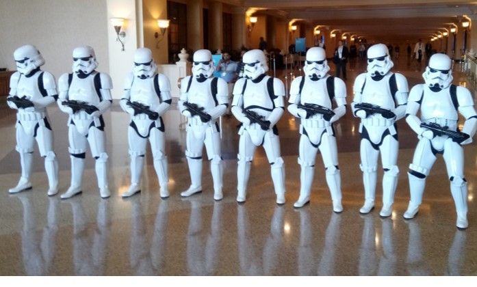 A line of eight Stormtroopers in white armor, holding blasters, standing in a lobby.