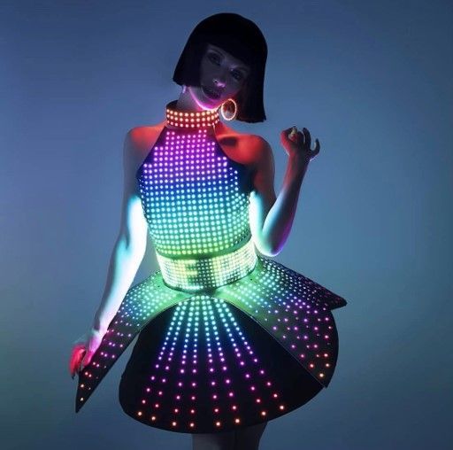 Woman wearing a vibrant LED dress with a halter top, belt, and flared skirt, lit against a blue background.
