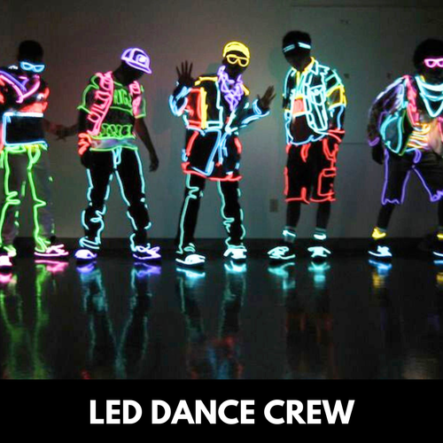 LED-lit dance crew performing on a reflective floor; neon outfits glow in various colors; black background.