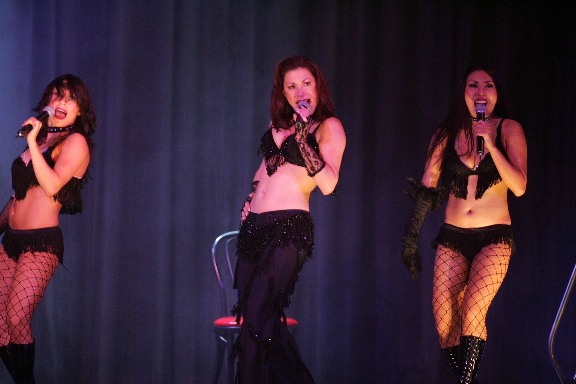 Three women in black lingerie sing on stage.