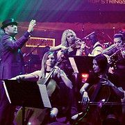 A conductor leads a string orchestra playing on stage.