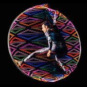 Performer within a large, colorful geometric hoop, black background.