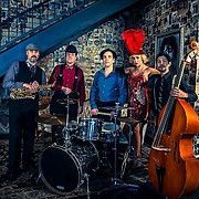 Jazz band performing in a vintage setting: saxophone, drums, bass, singer in red.