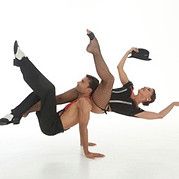 Acrobatic couple in dance poses; man on hands, woman balanced on him in black and red attire.
