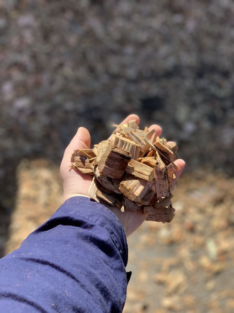 A Person Is Holding A Pile Of Wood Chips In Their Hand — Serious About Landscape Supplies In West Gosford, NSW