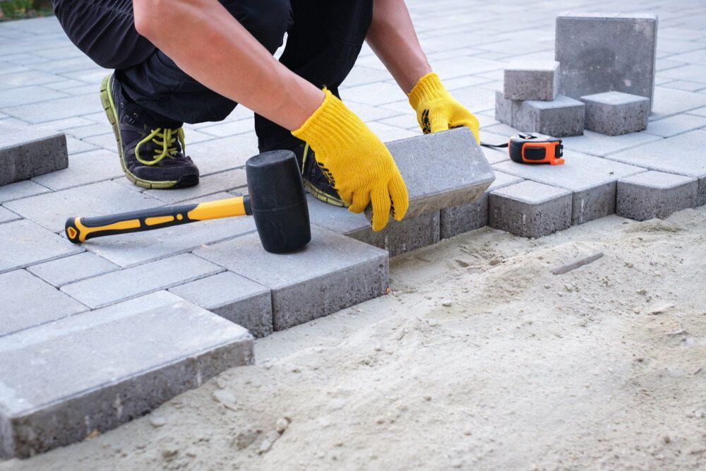 A Man Is Laying Bricks On A Patio With A Rubber Mallet — Serious About Landscape Supplies In West Gosford, NSW