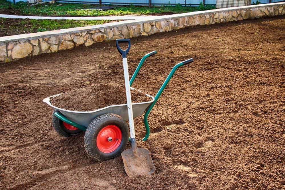A Wheelbarrow And Shovel Are Sitting On Top Of A Pile Of Dirt — Serious About Landscape Supplies In Terrigal, NSW