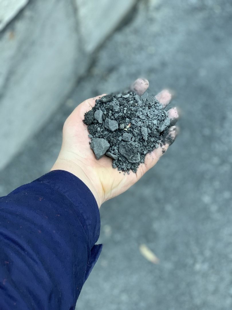A Person Is Holding A Pile Of Black Rocks In Their Hand — Serious About Landscape Supplies In West Gosford, NSW
