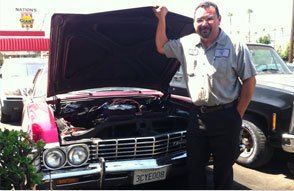 Man standing beside a classic black car with its hood open at an outdoor event | S.G. Auto Repair