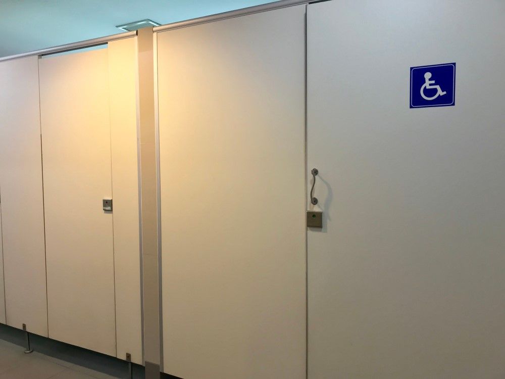 Bathroom stalls, one with accessibility symbol, white doors, metal trim.