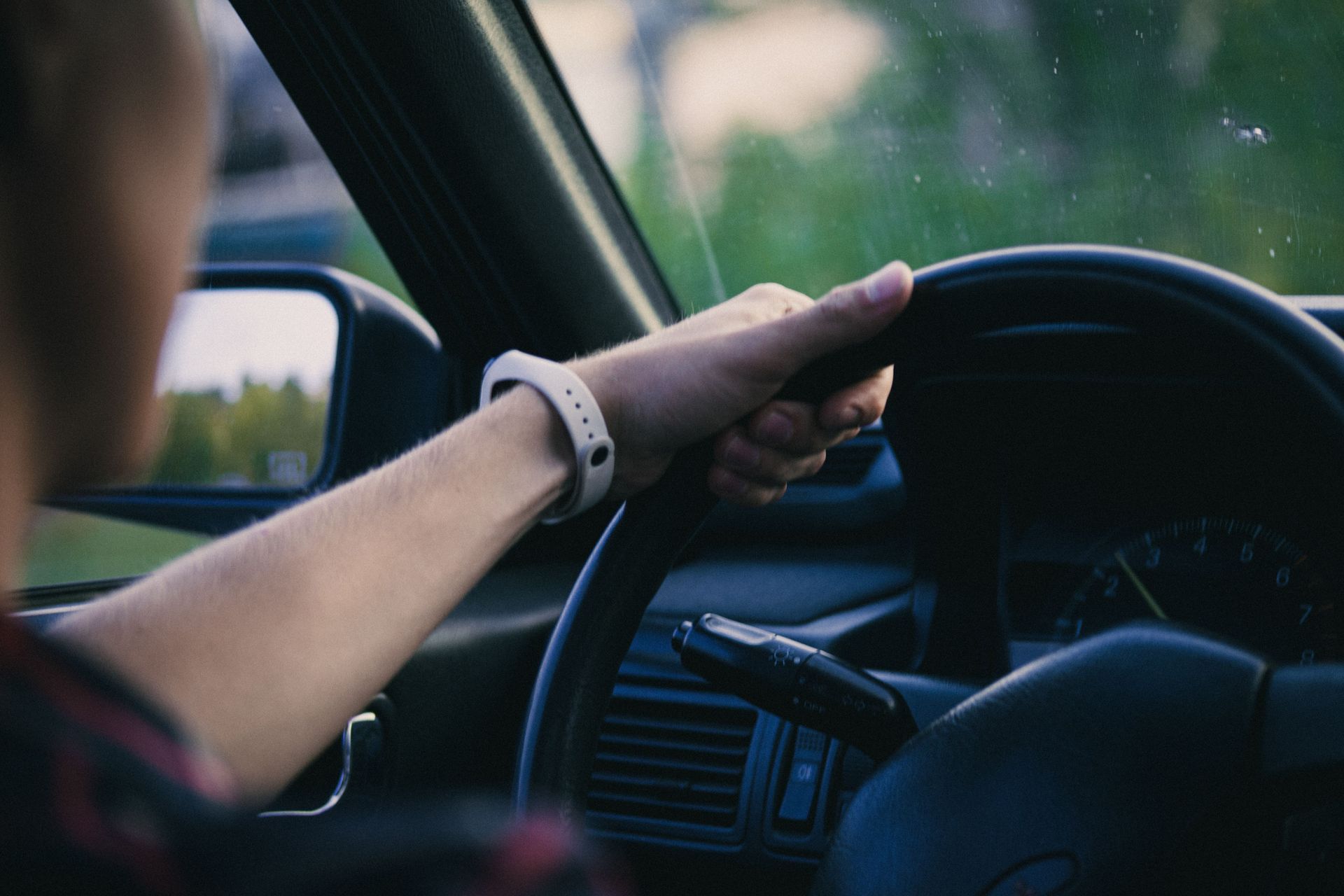 Driver’s hand on steering wheel inside a car, seen from the passenger seat.