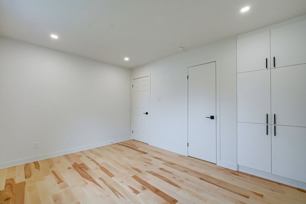 Pièce blanche vide avec parquet clair et placards blancs intégrés sous éclairage encastré au plafond