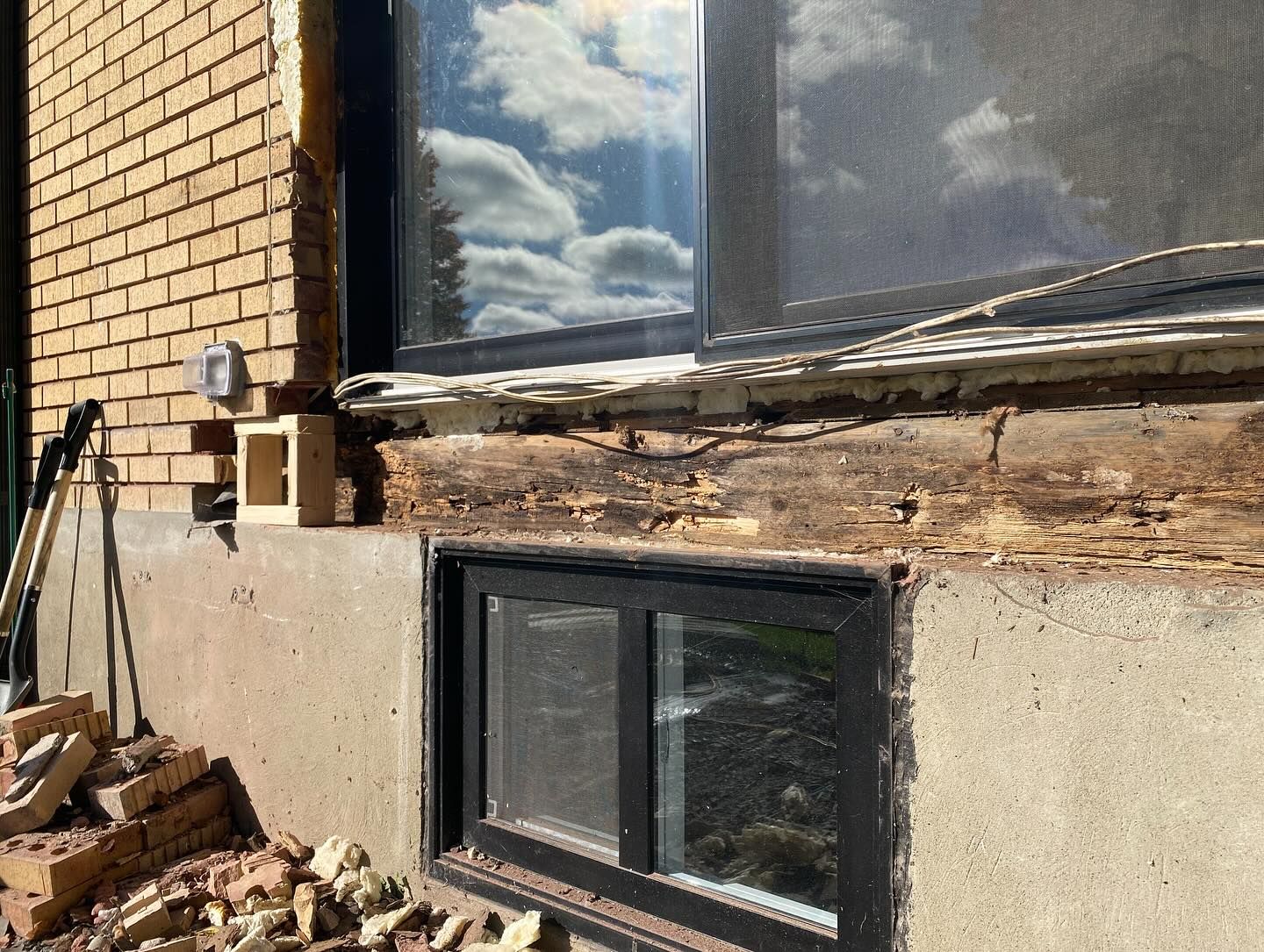 Mur extérieur avec moulures en bois endommagées au-dessus d'une fenêtre de sous-sol et revêtement en briques en cours de réparation