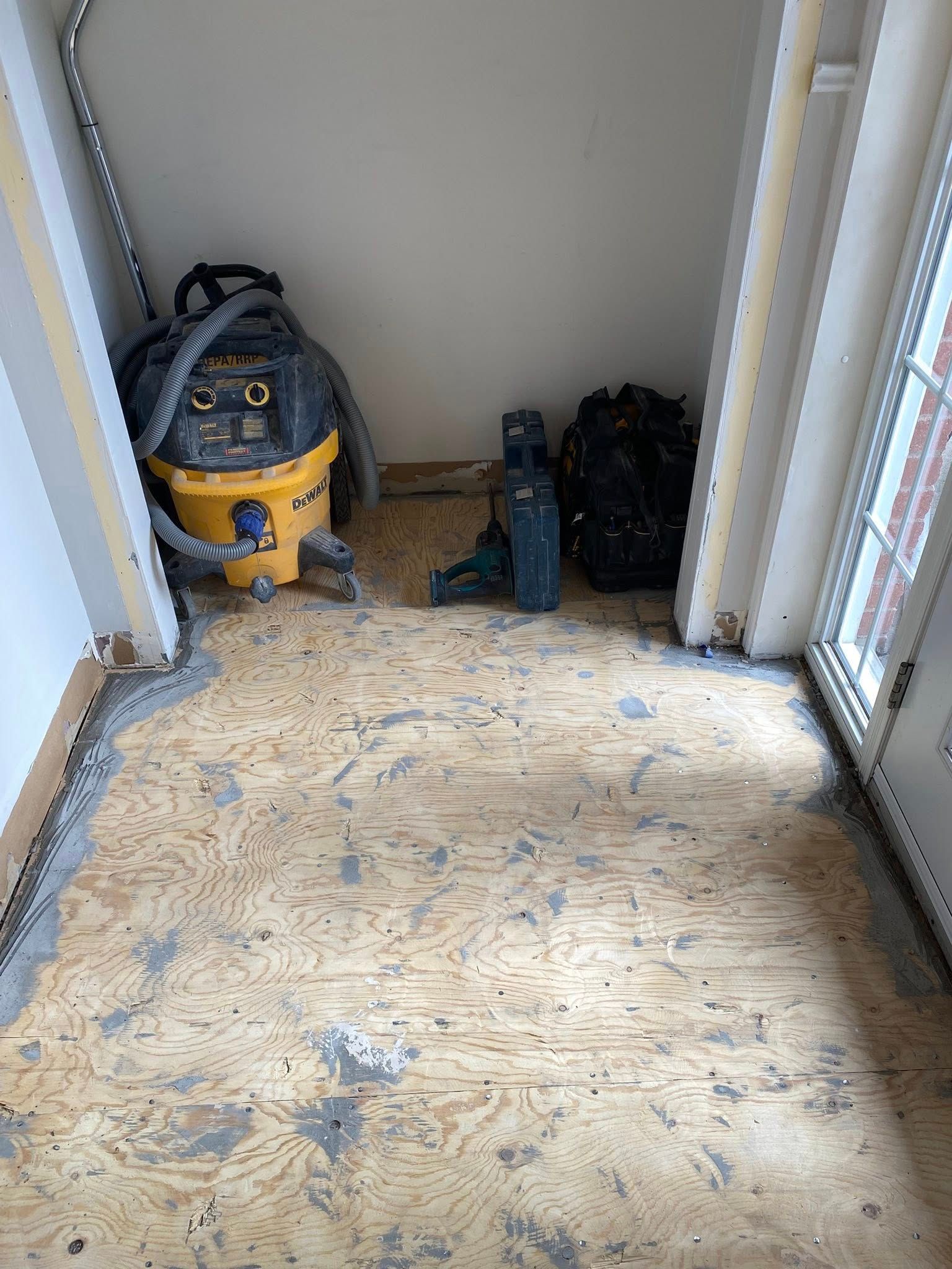 Petit placard contenant des outils de nettoyage, dont un aspirateur jaune, un outil bleu et des sacs posés au sol.