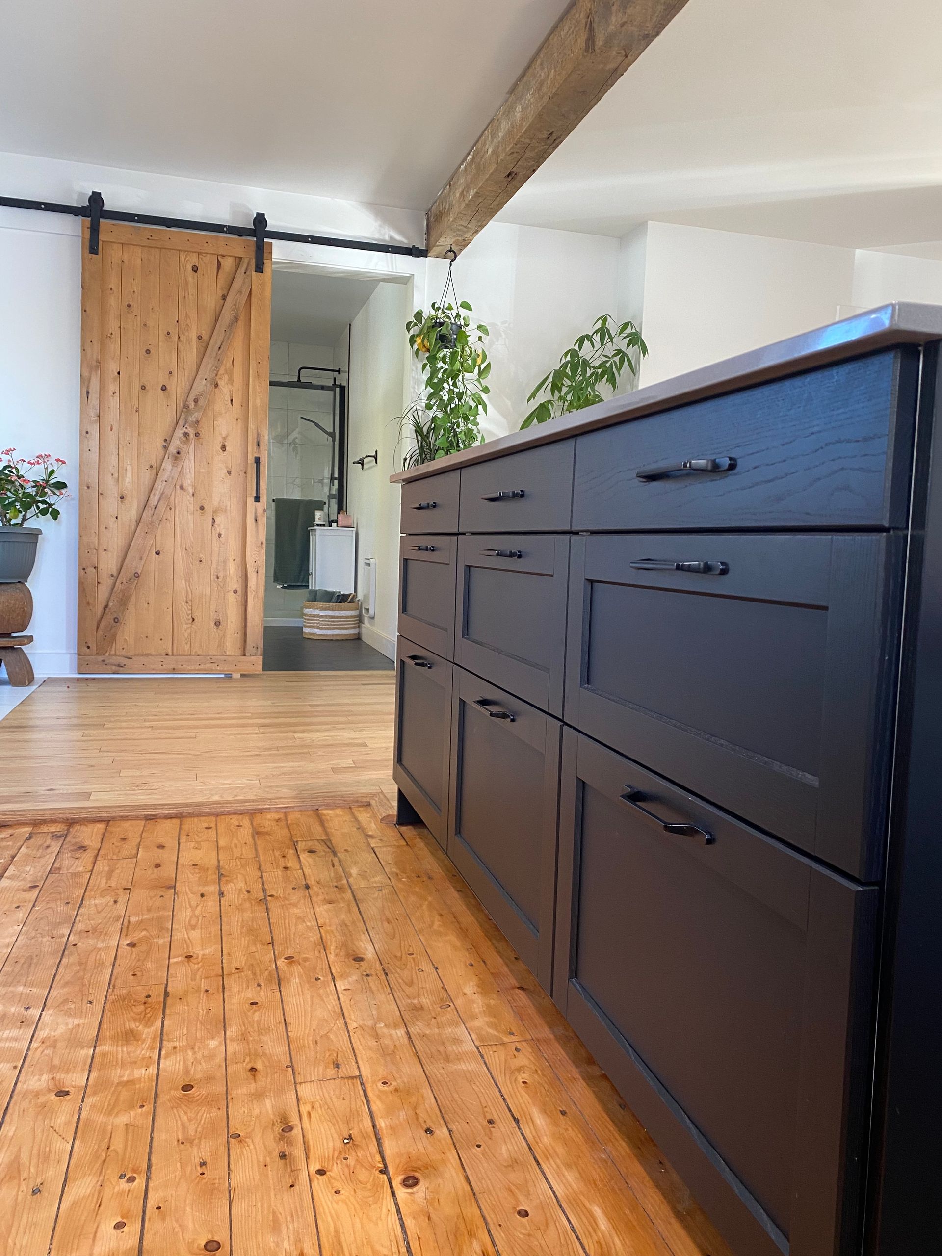 Intérieur avec commode bleu foncé sur parquet, poutre apparente et porte coulissante en bois en arrière-plan.