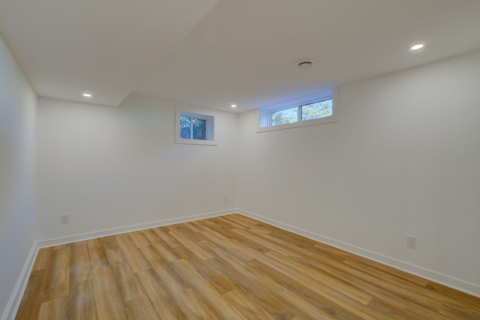Pièce blanche vide avec parquet clair et petites fenêtres hautes