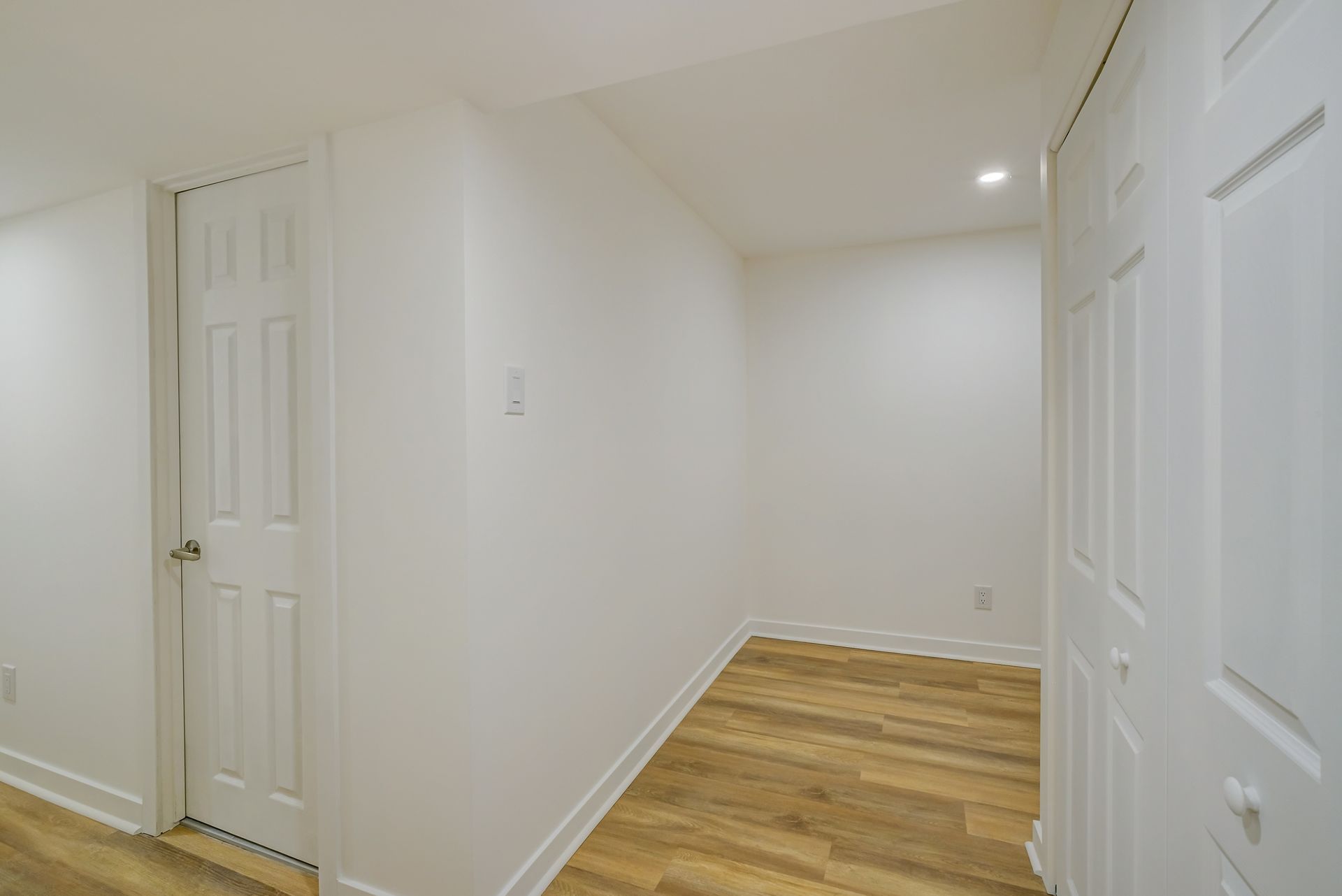Couloir étroit blanc avec parquet et plusieurs portes fermées
