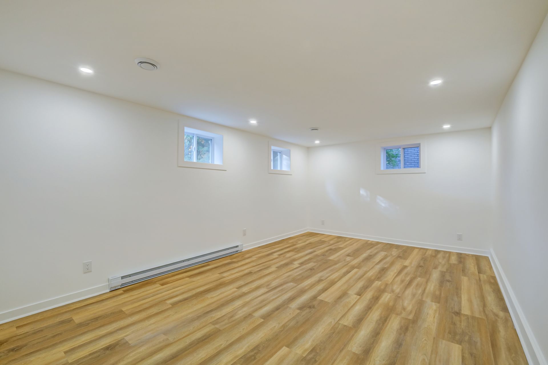 Pièce blanche vide avec parquet et petites fenêtres, éclairée par des spots encastrés au plafond