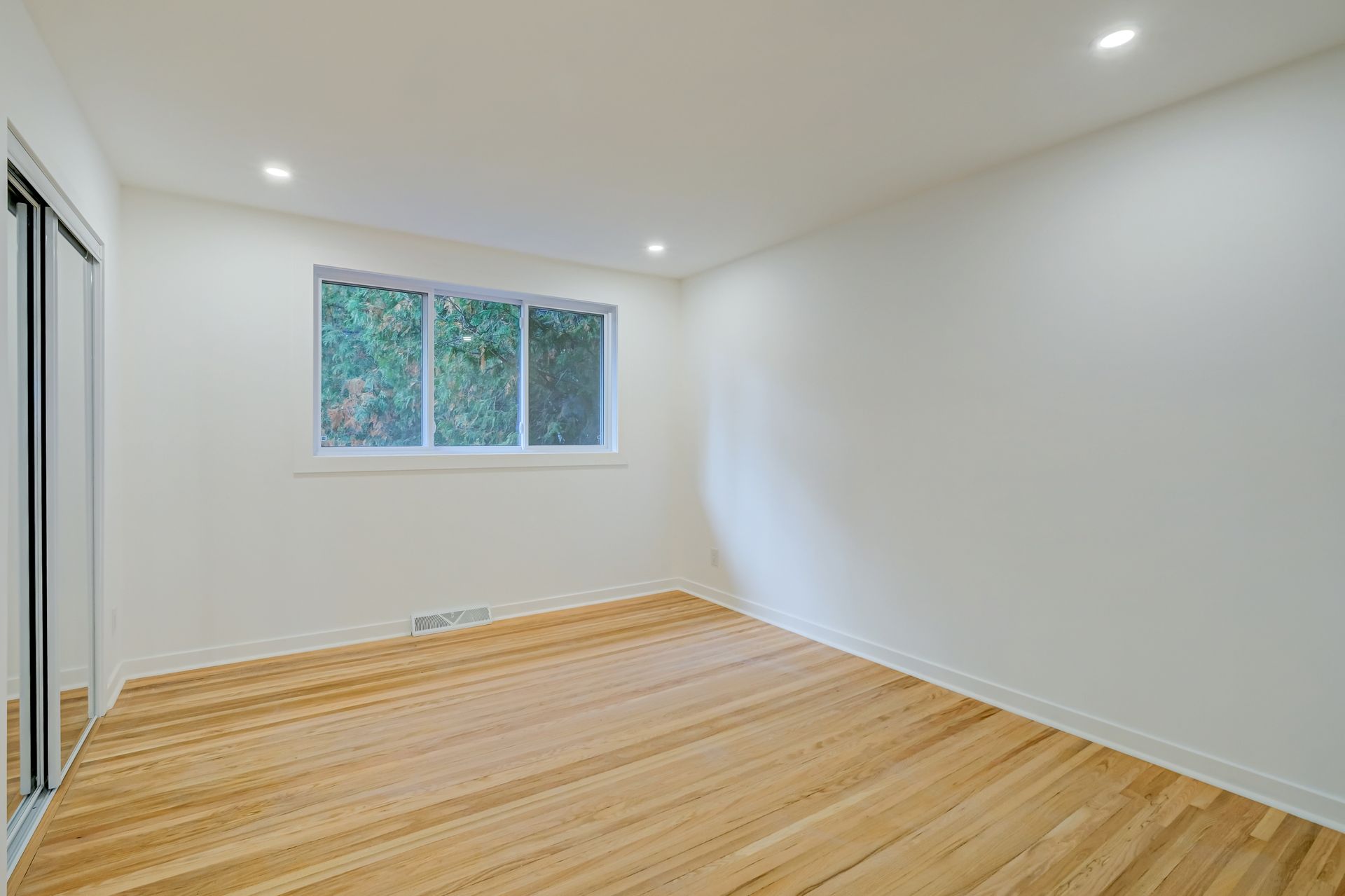 Chambre blanche vide avec parquet et petite fenêtre
