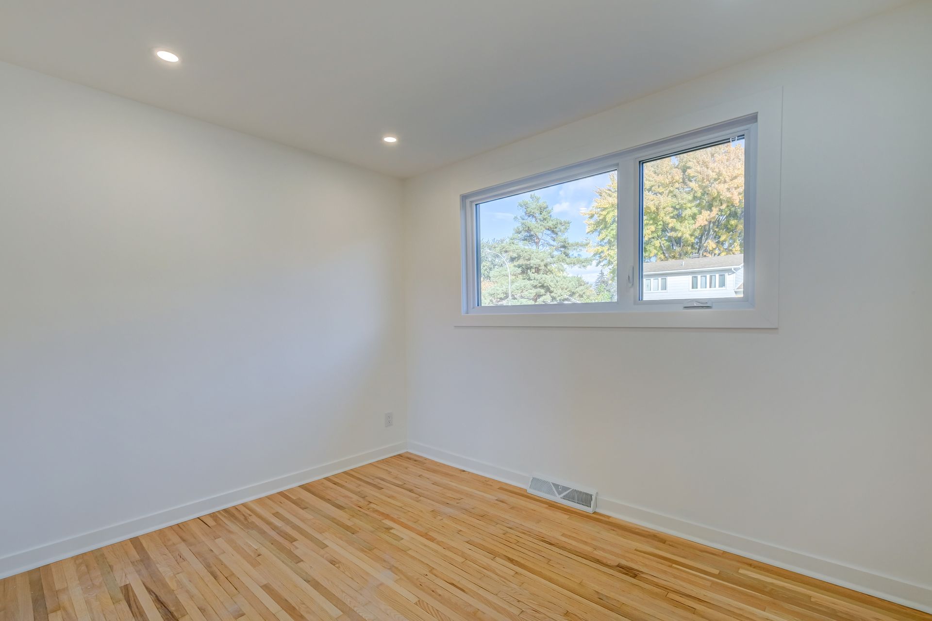 Chambre blanche vide avec parquet et deux fenêtres laissant entrer la lumière du jour