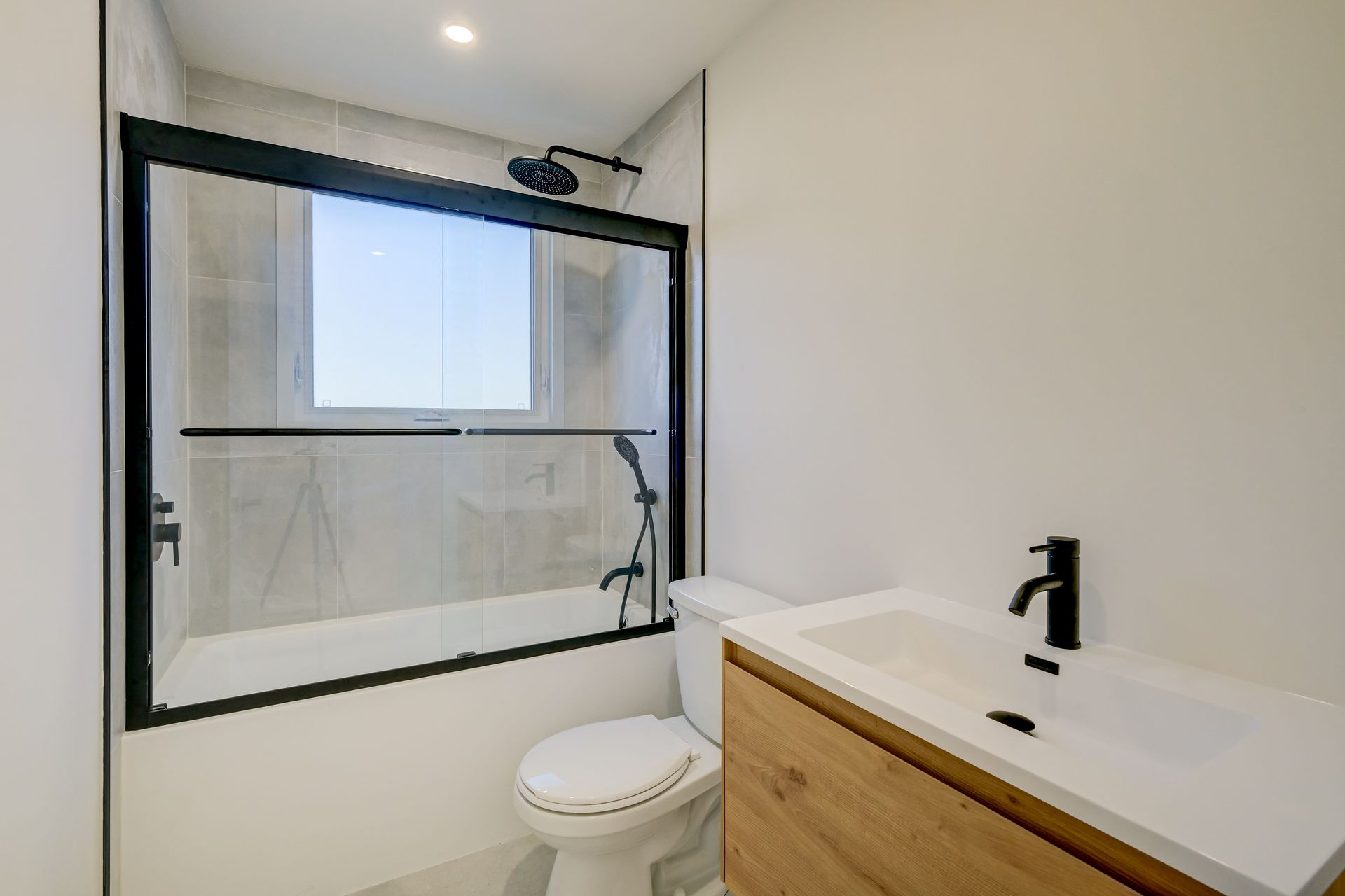 Salle de bains moderne avec douche à l'italienne en verre à cadre noir, murs blancs et meuble-lavabo en bois.