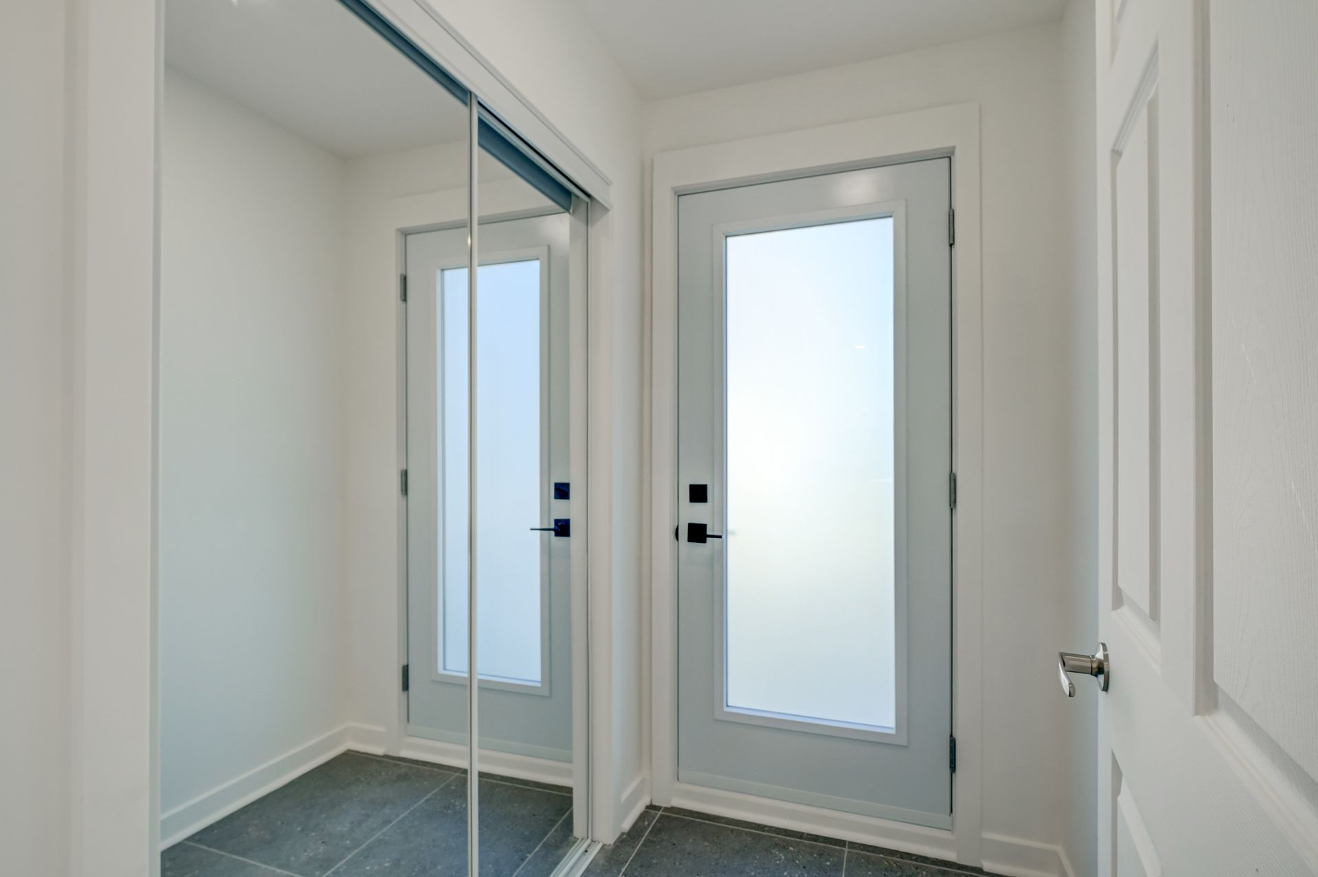Entrée lumineuse avec portes de placard à miroir et une porte blanche sur un sol carrelé.