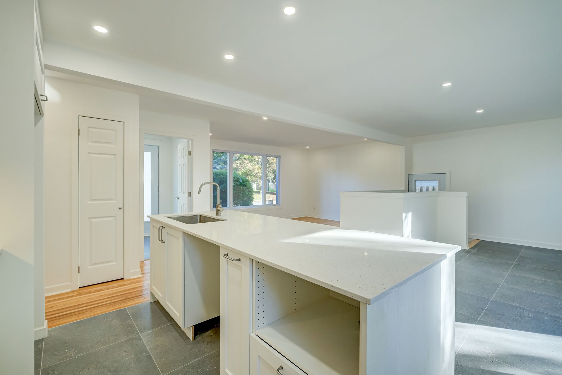 Cuisine moderne, lumineuse et épurée, avec îlot central blanc, spots encastrés et carrelage gris au sol.