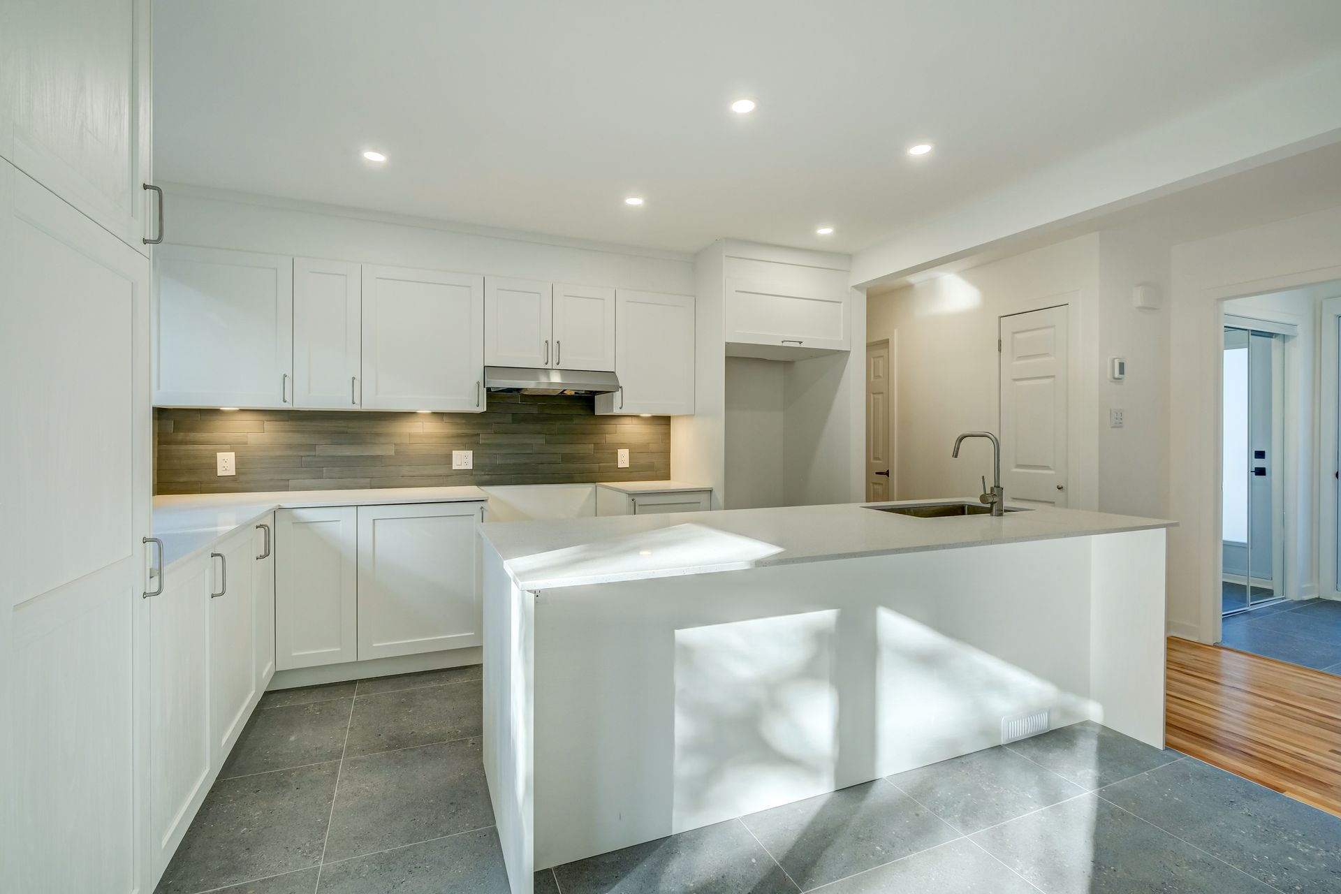 Cuisine moderne et lumineuse d'un blanc éclatant avec îlot central, éclairage intégré et parquet clair.