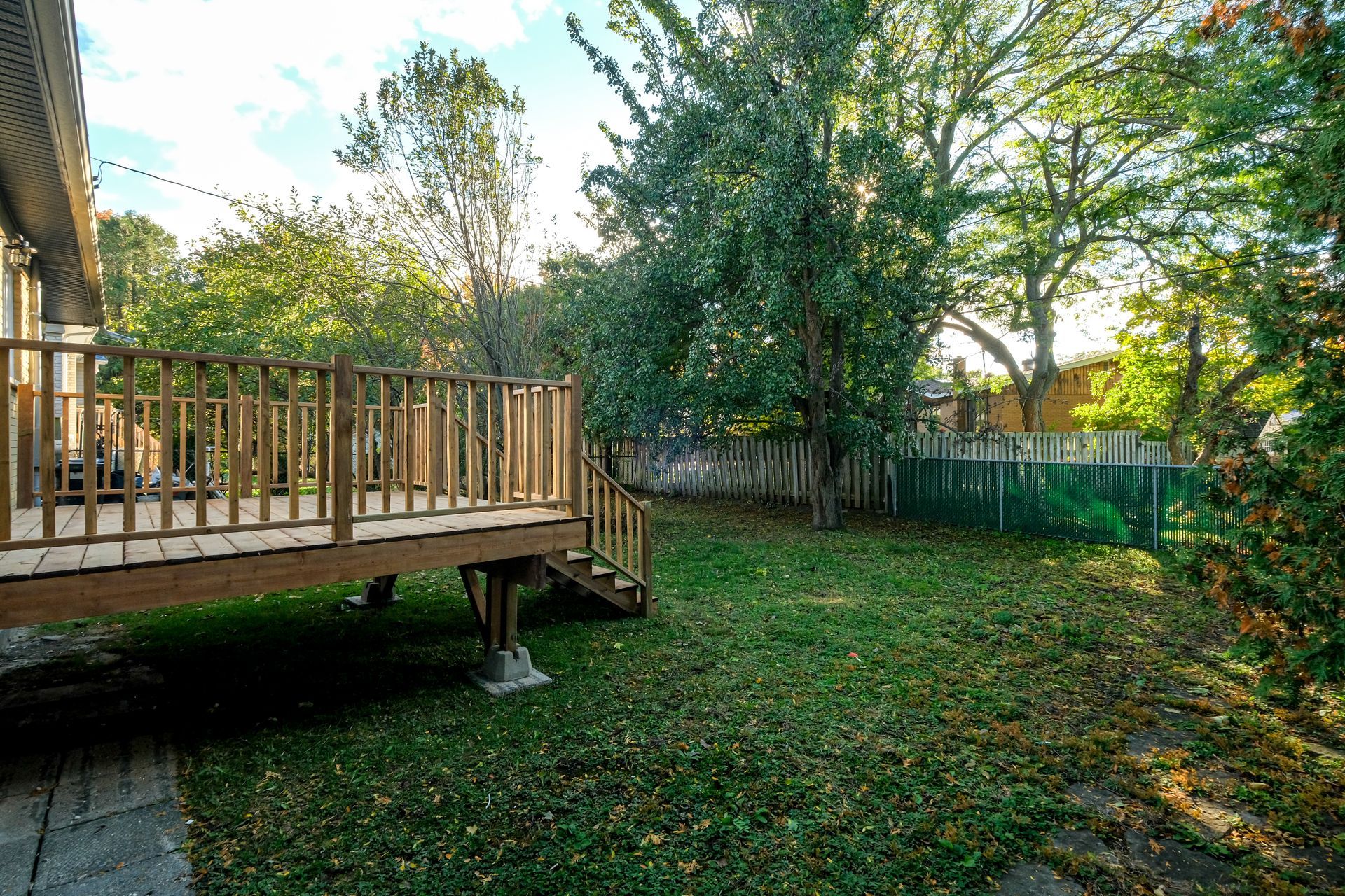 Terrasse en bois donnant sur un jardin gazonné avec des arbres et une clôture au coucher du soleil