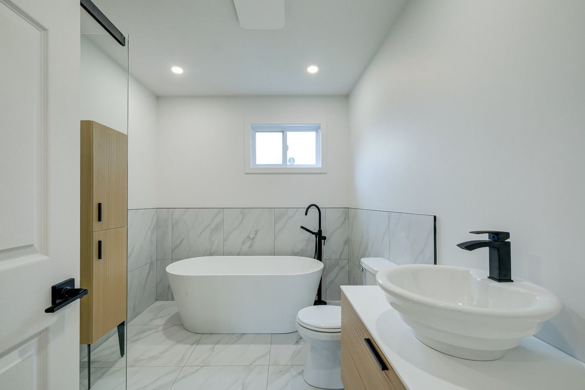 Salle de bains moderne et lumineuse avec baignoire îlot, robinetterie noire, carrelage en marbre et double vasque.