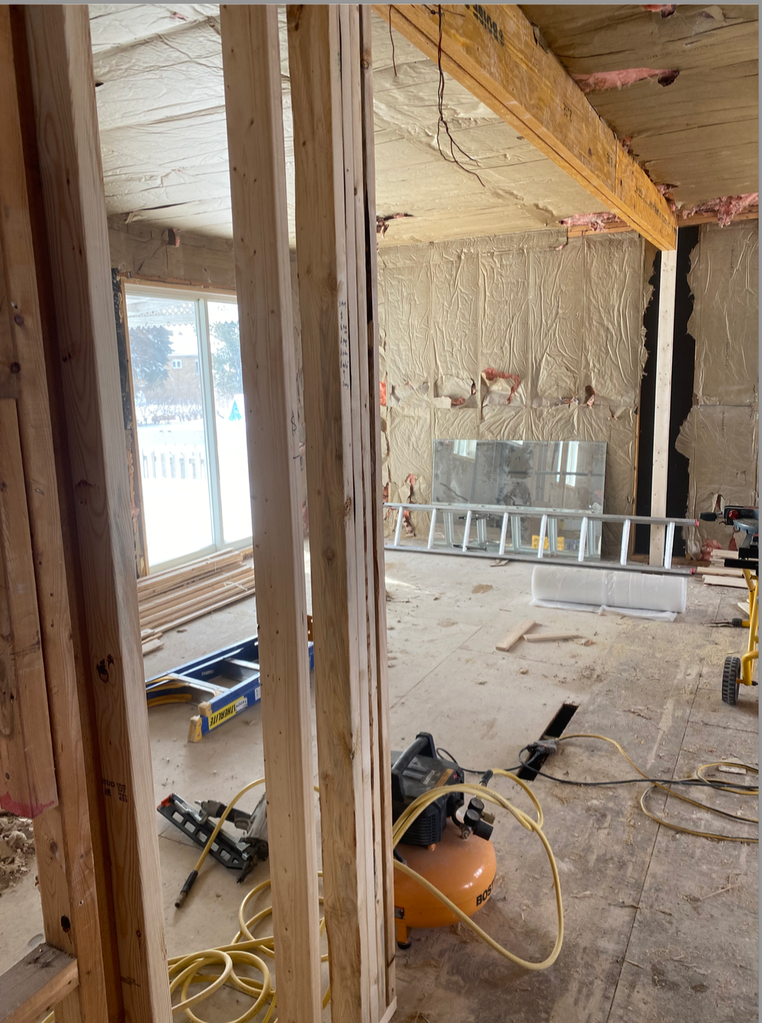 Chantier de rénovation avec charpente apparente, isolation, outils et une fenêtre dans une pièce partiellement démolie