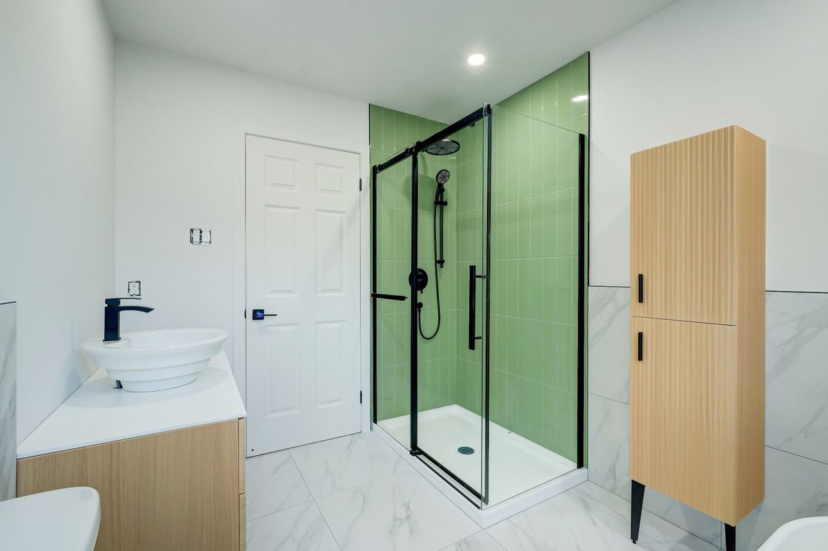 Salle de bains moderne et lumineuse avec lavabo blanc, douche en verre à cadre noir et meuble en bois clair sur sol en marbre