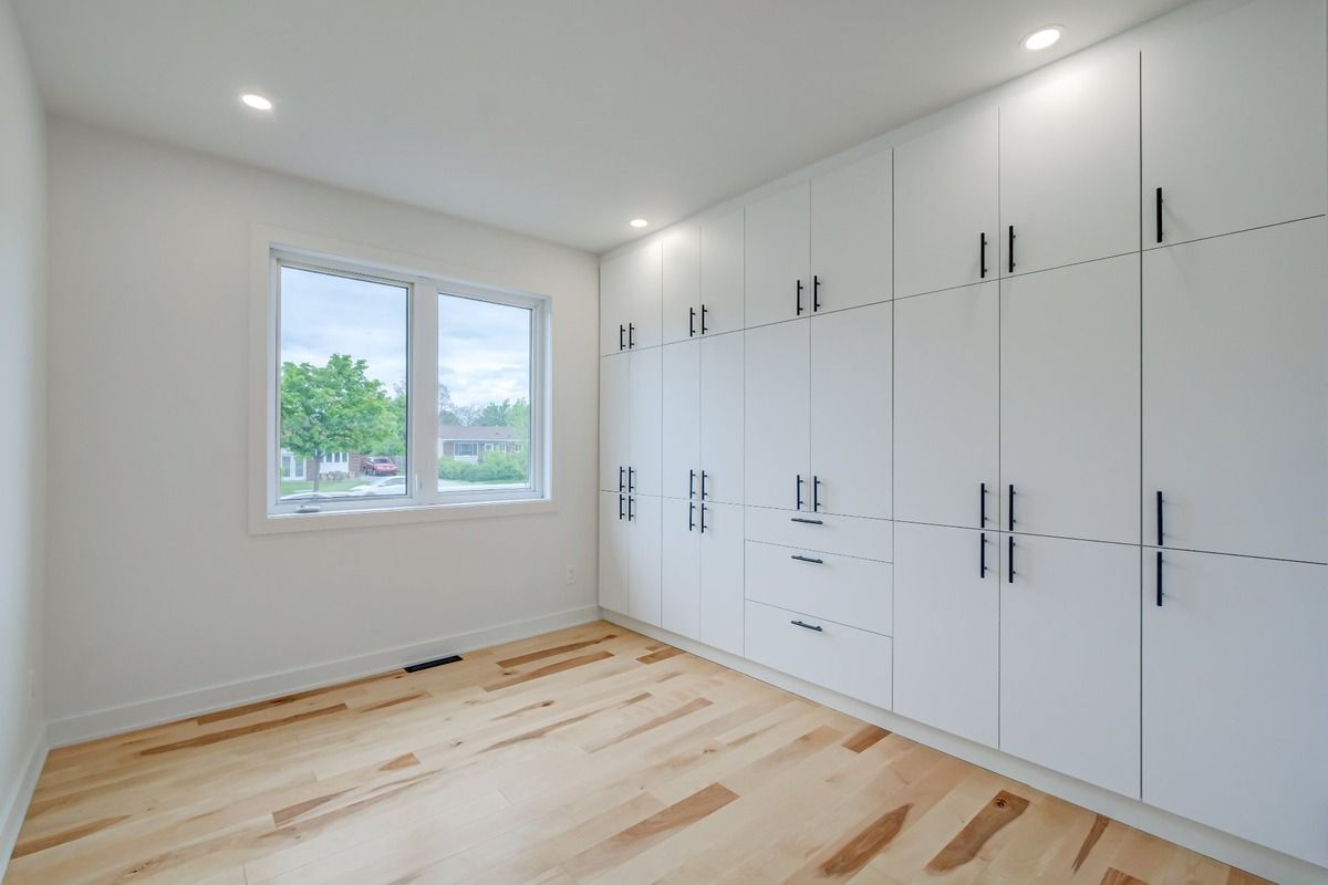 Chambre blanche lumineuse avec placards intégrés, parquet clair et fenêtre donnant sur les arbres