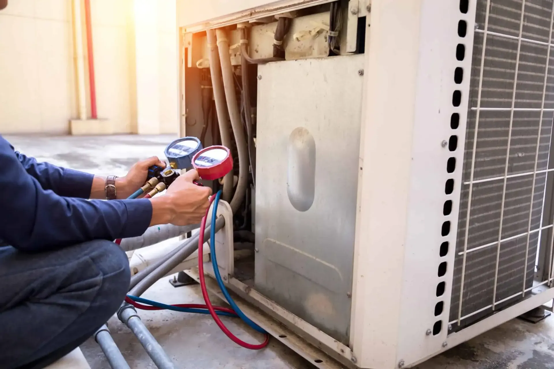 HVAC technician servicing an air conditioning unit, using gauges to check pressure.