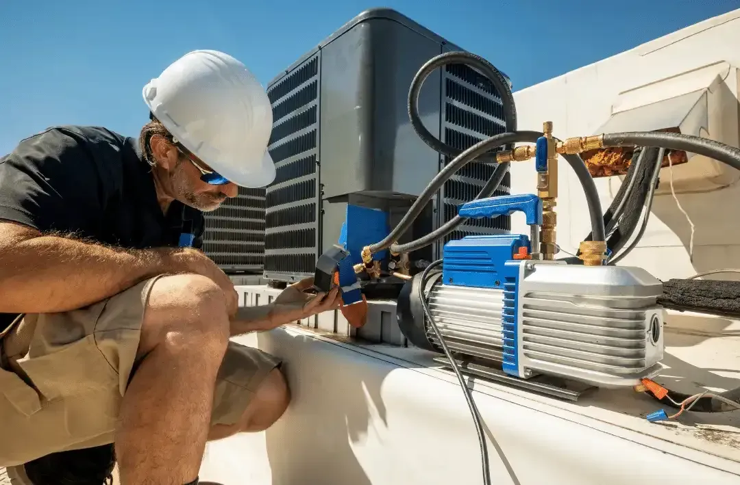 HVAC technician in hard hat on a roof, working on air conditioning unit.
