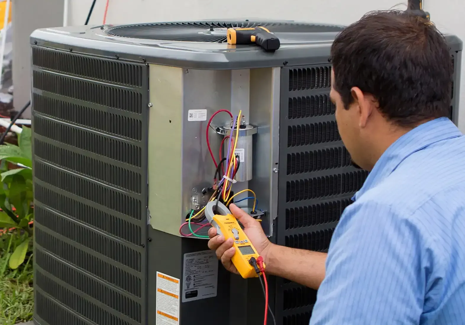 HVAC technician using a meter on an air conditioner unit outside.