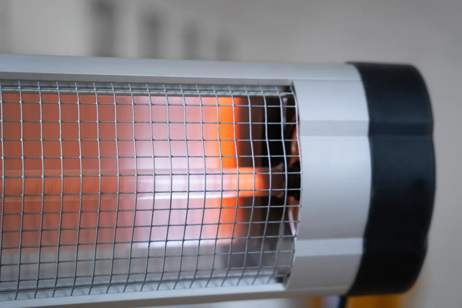 Close-up of a silver electric heater with a wire mesh covering an orange heating element. Black end cap.