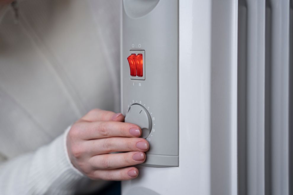 Hand adjusting the temperature dial on a white oil-filled radiator with the red power switch lit.